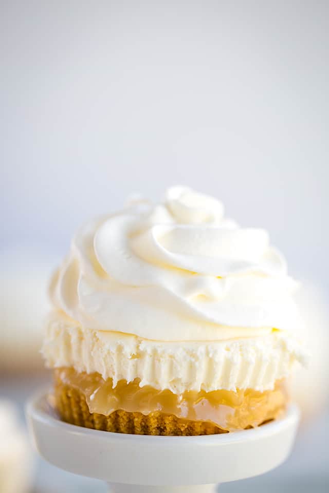 close up of no bake lemon cheesecake with the lemon curd coming out the sides on a white cupcake stand