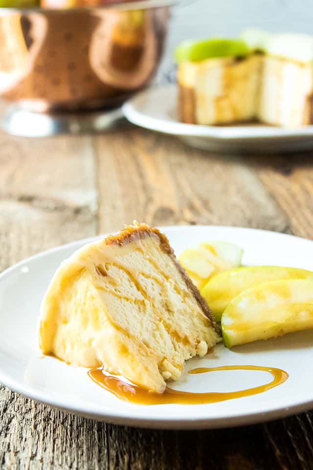 Slice of instant pot caramel apple cheesecake on white plate with cheesecake in background