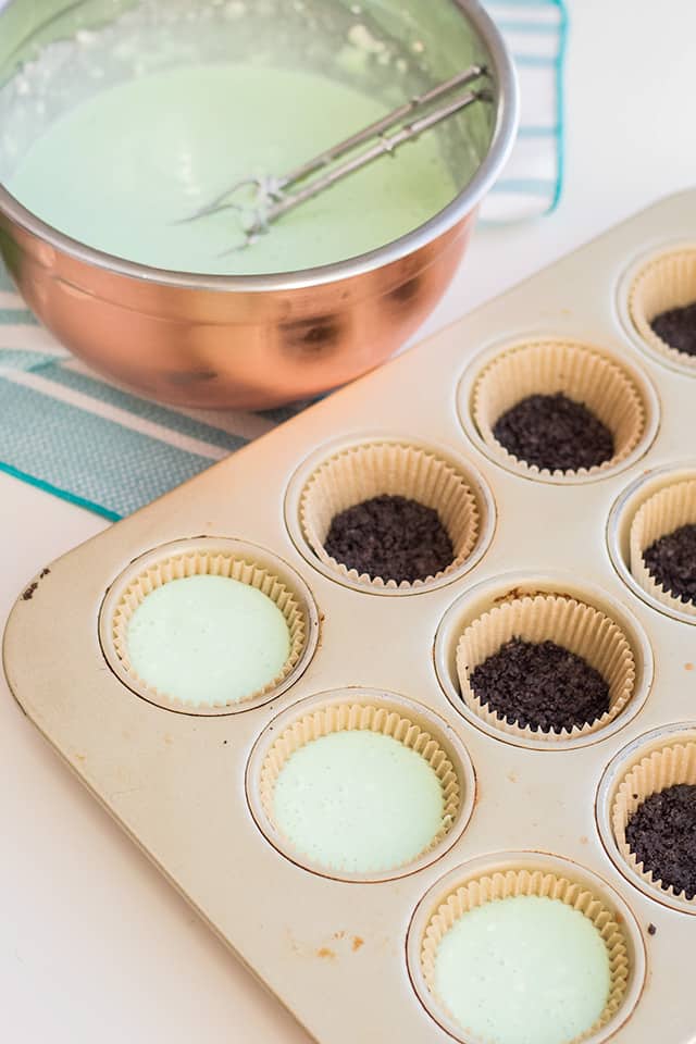 adding mint cheesecake batter to a cupcake pan with a mint oreo crust