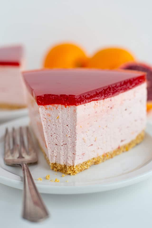 bite taken out of blood orange cheesecake slice that's on a dessert plate with fork