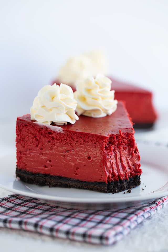 red velvet cheesecake on a plate with a plaid fabric with a bite taken out of the cheesecake