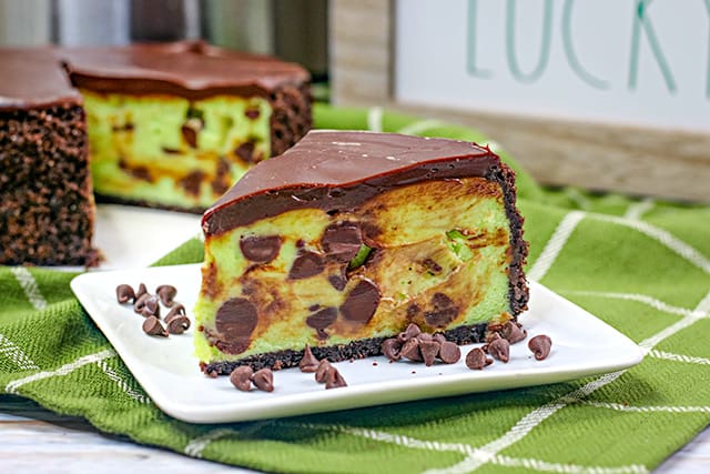 photo of mint chip cheesecake on a white square plate with chocolate chips and a green linen under the plate