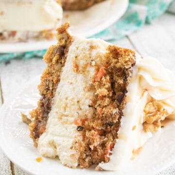 closeup of carrot cake cheesecake cake on a white plate with cake behind it