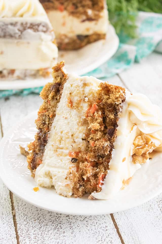 closeup of carrot cake cheesecake cake on a white plate with cake behind it