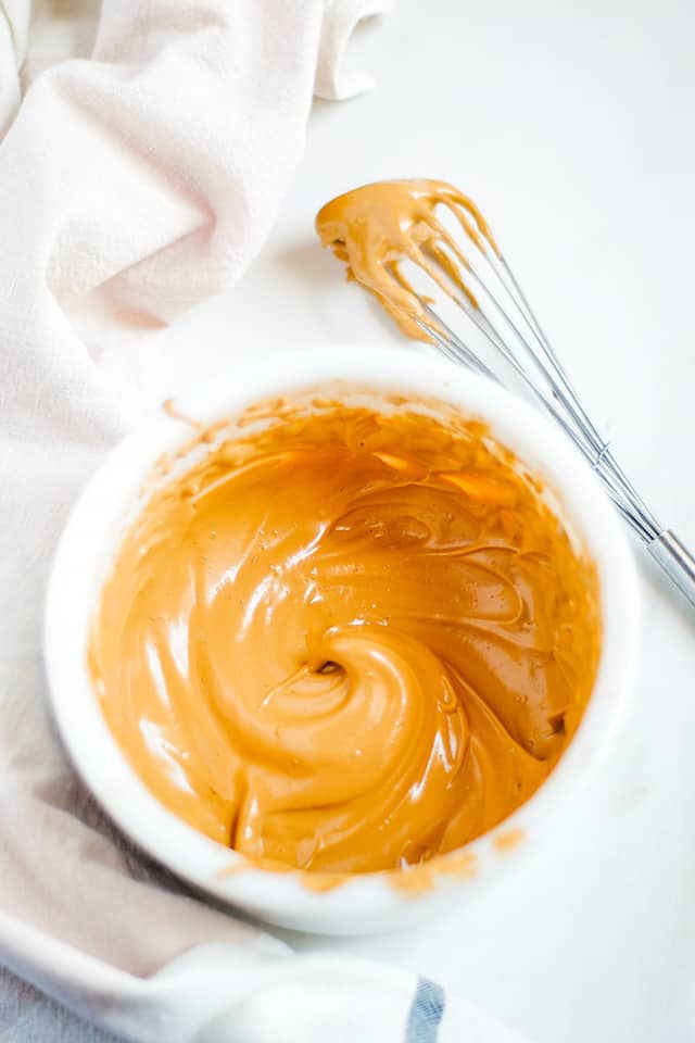 whipped coffee in a white bowl with a whisk beside the bowl