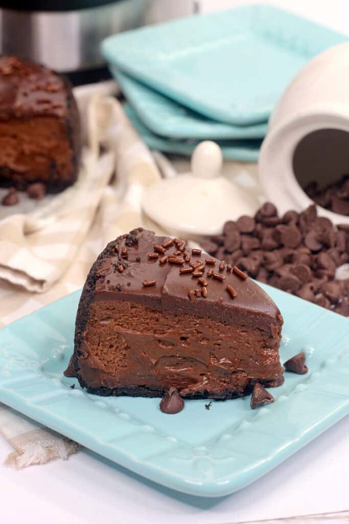 cheesecake on a blue square plate with chocolate chips behind it and a white jar