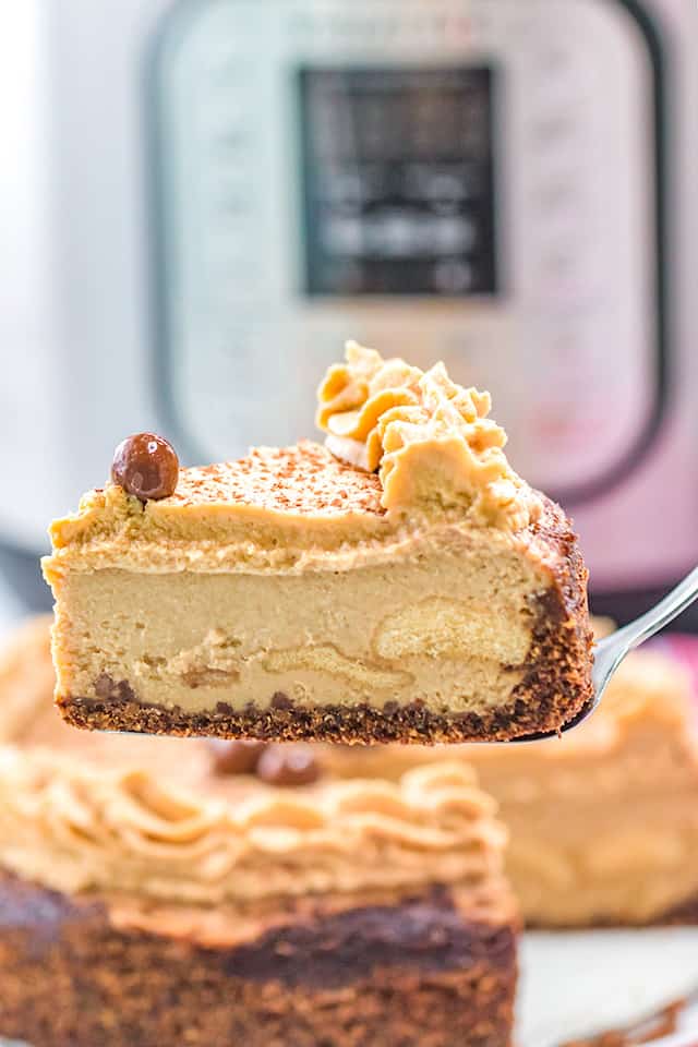 Pie server holding a slice of tiramisu cheesecake with an instant pot in the background