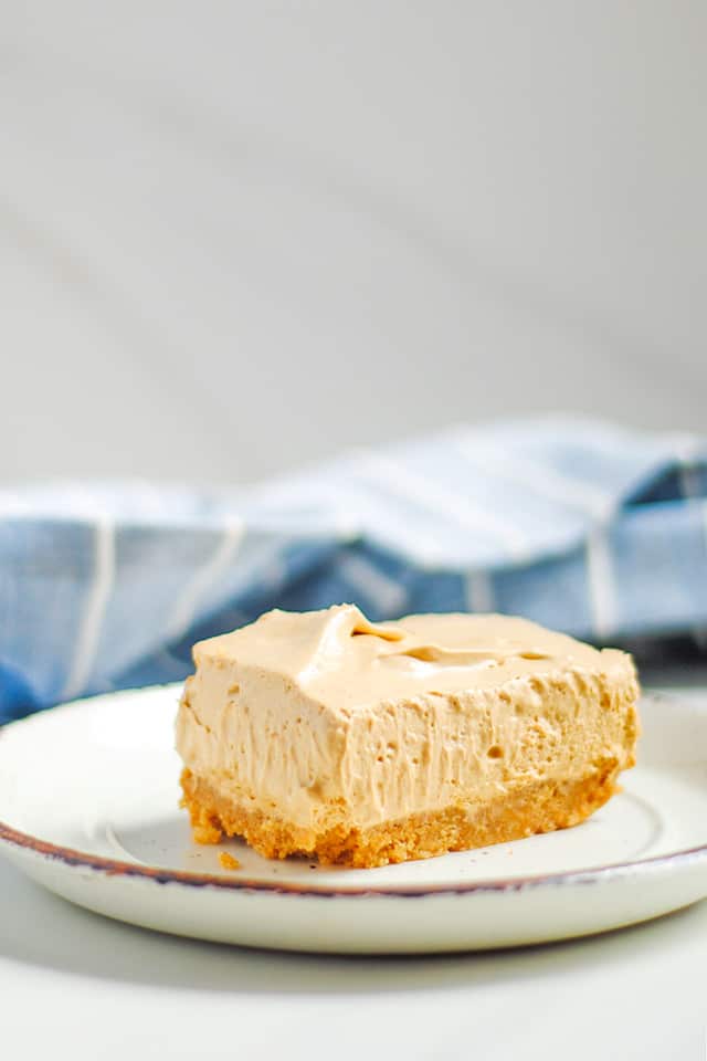 slice of dalgona coffee cheesecake bars on a white dessert plate with blue linen