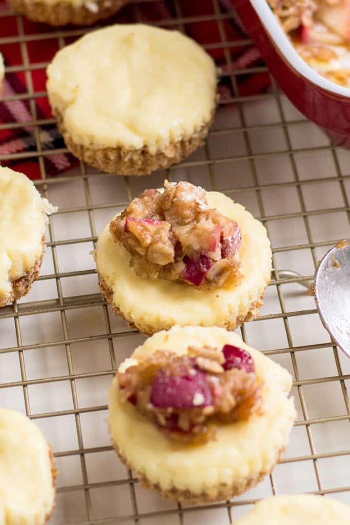 cheesecakes on a wire rack with apple crumble being added to the top