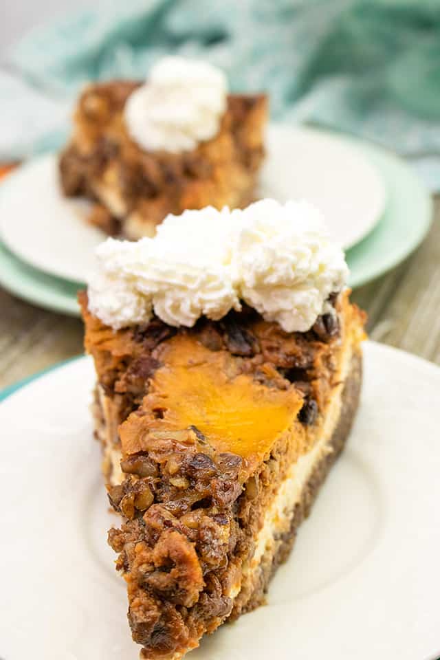 close up of a pocket of pecan pie topping on a slice of cheesecake that's on a white plate with a second slice of cheesecake behind it