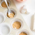 muffin pan with cupcake liners and graham cracker crusts in it