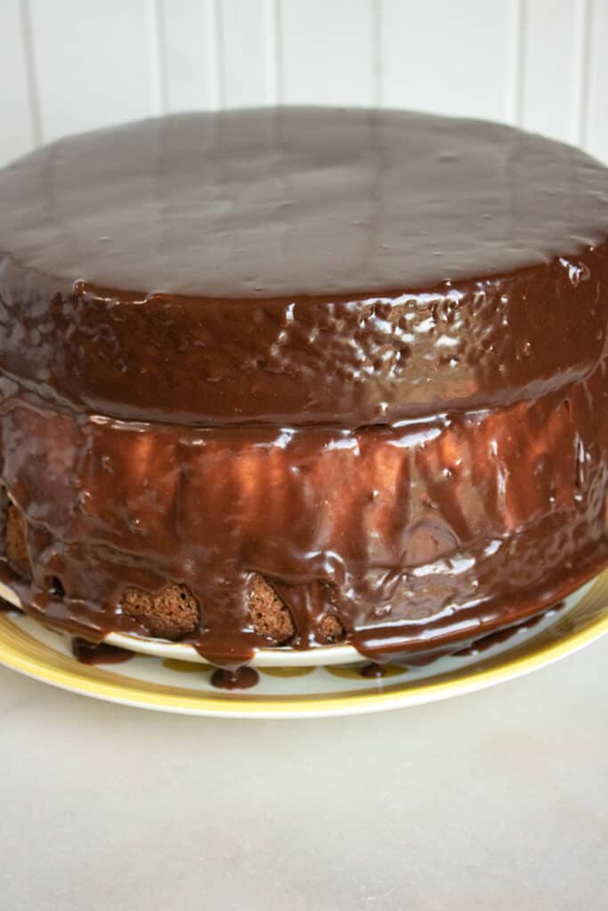 a cheesecake cake covered in ganache on a yellow rimmed plate