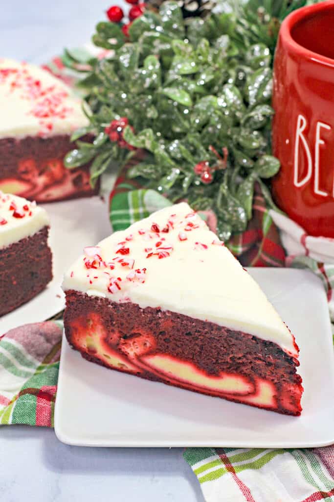 slice of cheesecake cake on a square white plate with greenery behind it