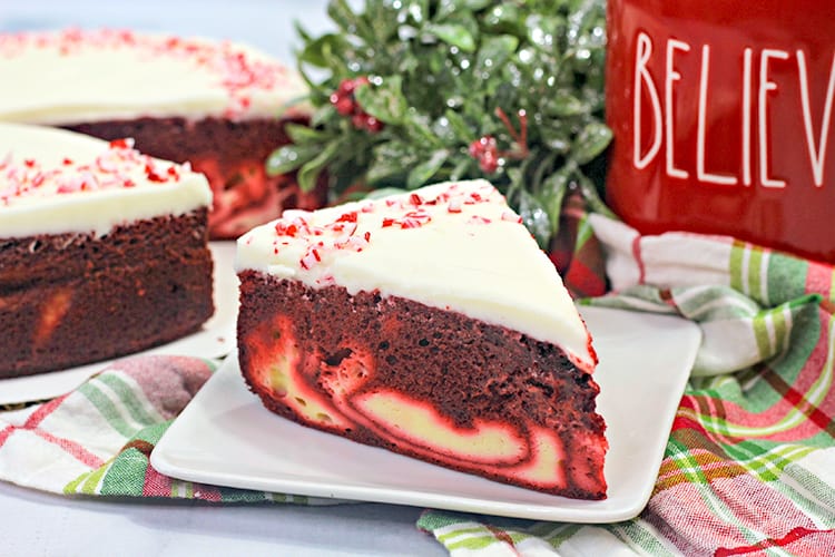 horizontal photo showing the cheesecake cake on a white plate with a red and green fabric and the rest of the cheesecake behind it