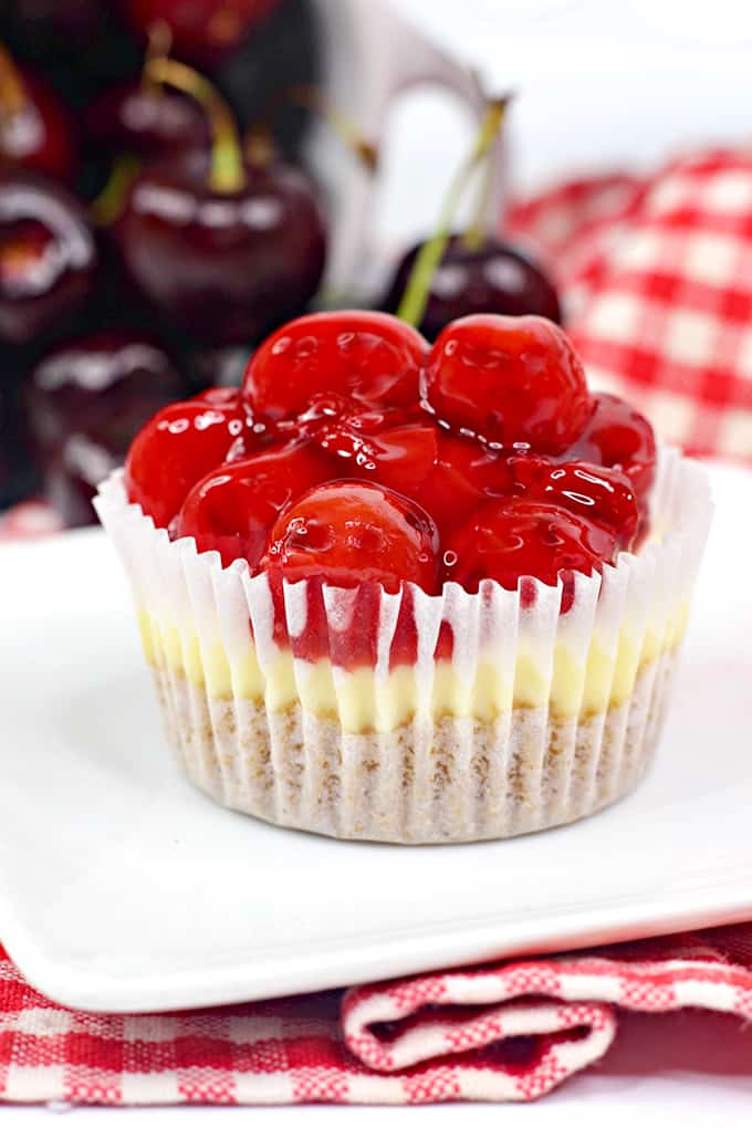 close up of a mini cheesecake cupcake in its paper liner with real cherries behind the cheesecake