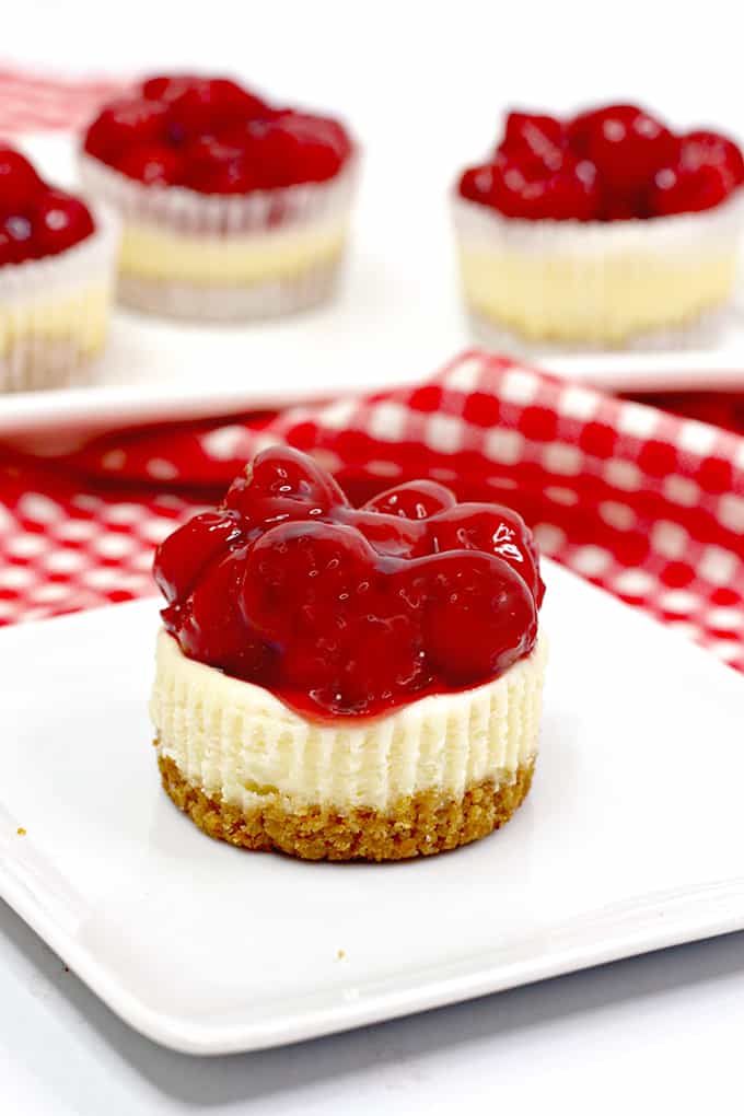 cheesecake cupcake on a white plate with other cheesecakes behind in on a white platter