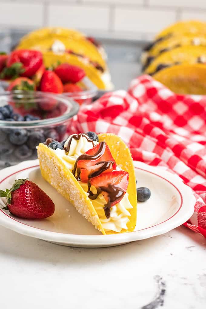 cheesecake tacos on a white plate with a blueberry and strawberry