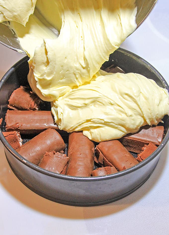 pouring cheesecake batter on top of swiss rolls and an oreo crust 