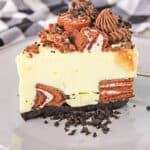 a slice of cheesecake on a gray plate with oreo crumbs beside the slice