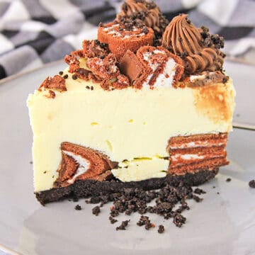 a slice of cheesecake on a gray plate with oreo crumbs beside the slice