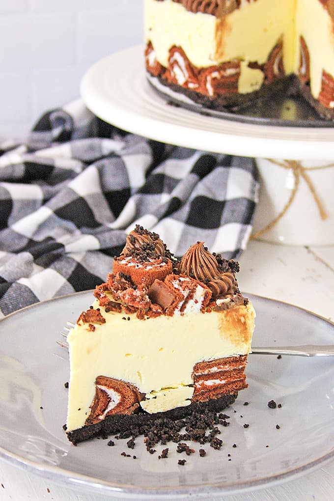 slice of cheesecake on a gray plate with a plaid linen behind it