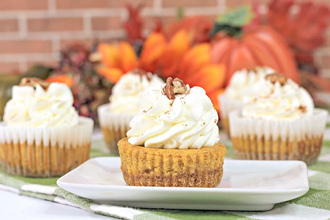 horizontal photo of the cheesecakes on a green checkered fabric with brick behind the cheesecakes