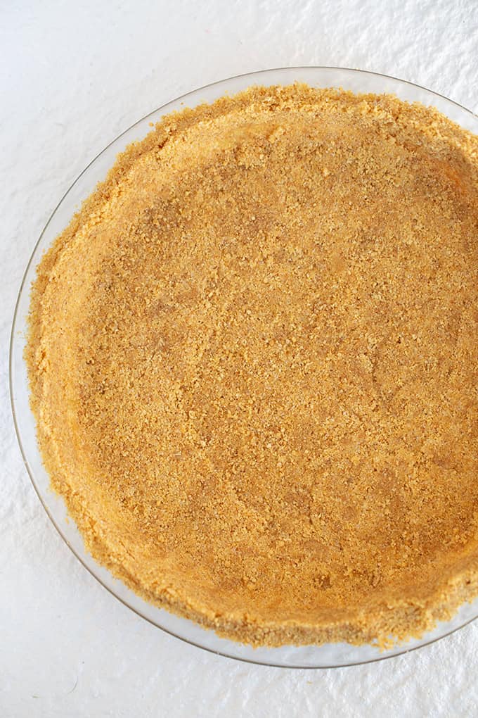 clear pie plate filled with a homemade graham cracker crust on a textured white table