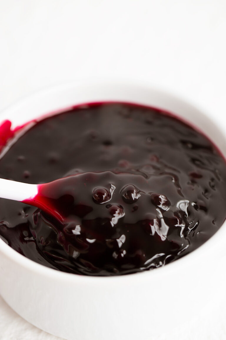 a white bowl with blueberry sauce in it and a white spoon filled with blueberry sauce in it